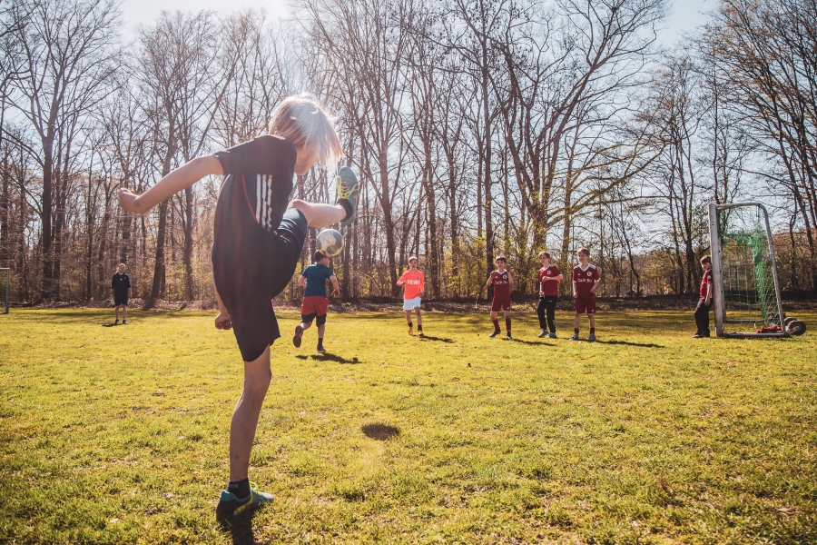 Jugendlicher beim Torschuss-Training mit Mitspielern im Hintergrund